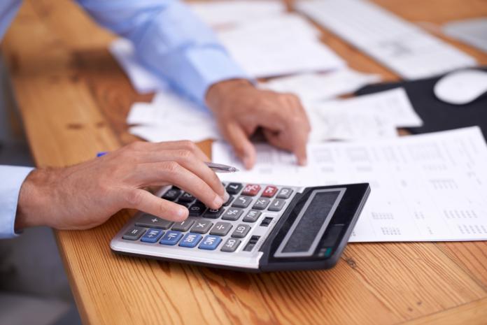Man with calculator using different types of invoice for his string of small businesses